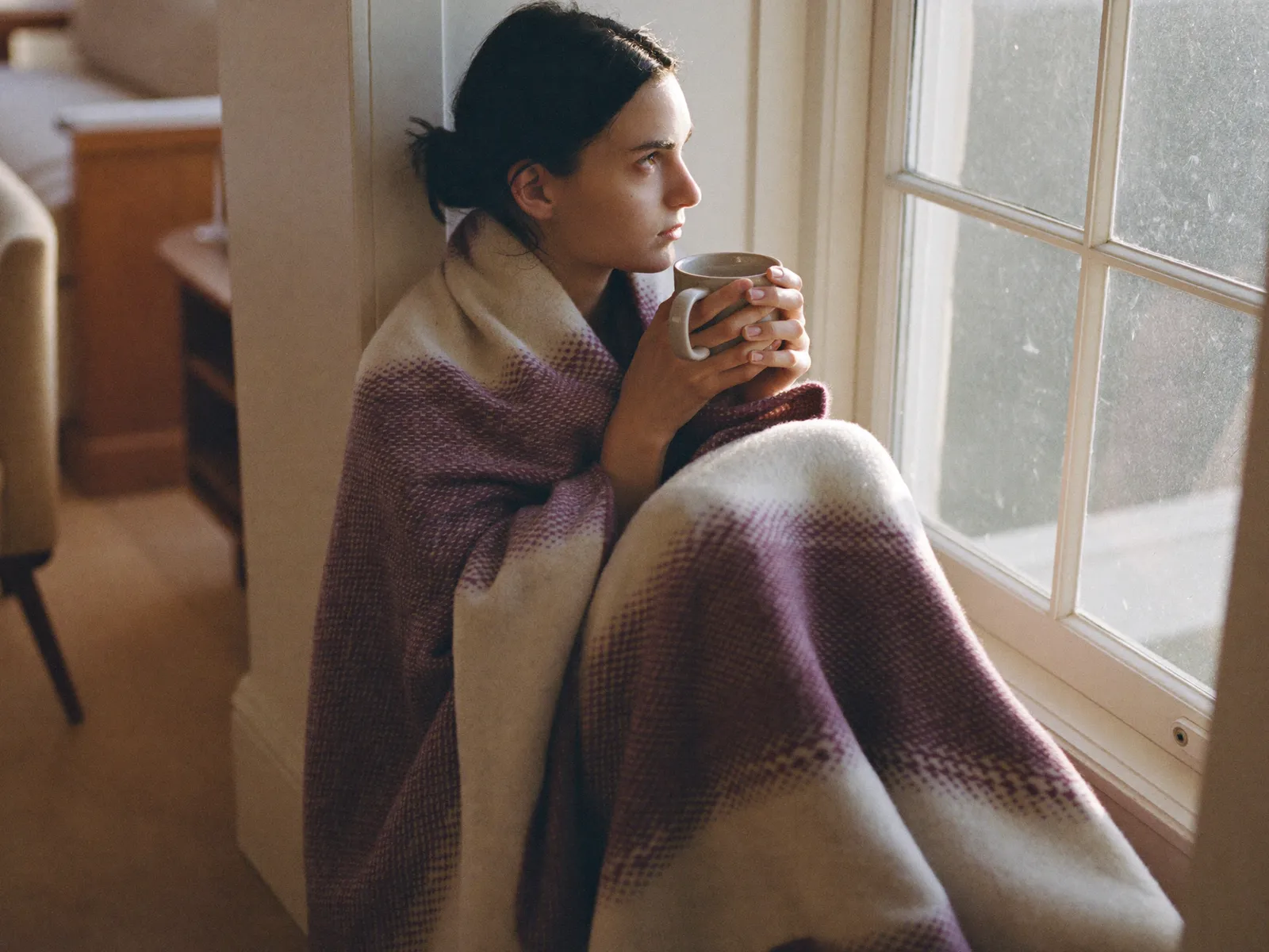A person sitting quietly by a window with a warm drink